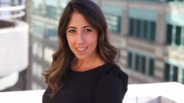 Woman with long hair smiling on a rooftop with a city building in the background.