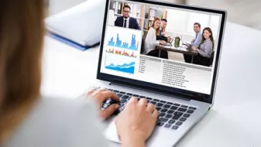Person attending a virtual meeting with graphs on laptop screen.