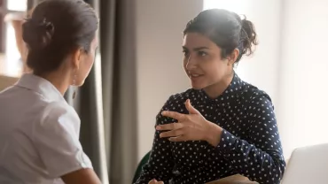 Two women having a discussion at a desk with a laptop.