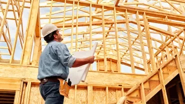 Builder holding plans at a wooden frame construction site.
