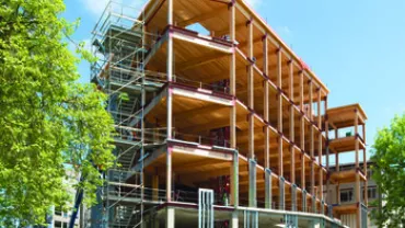 Partially constructed building with scaffolding and cranes under a blue sky.