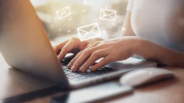 Hands typing on a laptop with floating email icons.