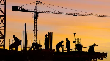 Silhouettes of construction workers and a crane at sunset.