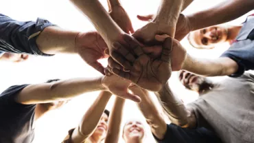 Diverse group of people in a circle with hands stacked in unity.