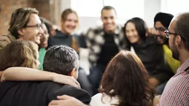 A group of people sitting close together in a circle, smiling and showing camaraderie.