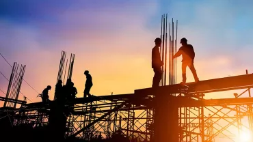 Silhouetted construction workers on scaffolding at sunset