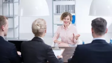Woman smiling during a job interview with a panel of interviewers in an office.