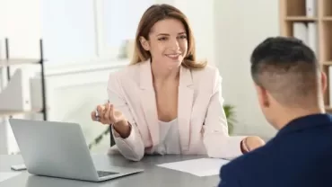 Woman in a business meeting with a laptop, smiling at a colleague.