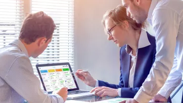Three colleagues reviewing a project on a laptop in a bright office.