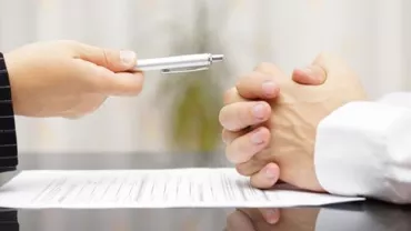 Two people sitting at a desk, a contract and pen in focus.