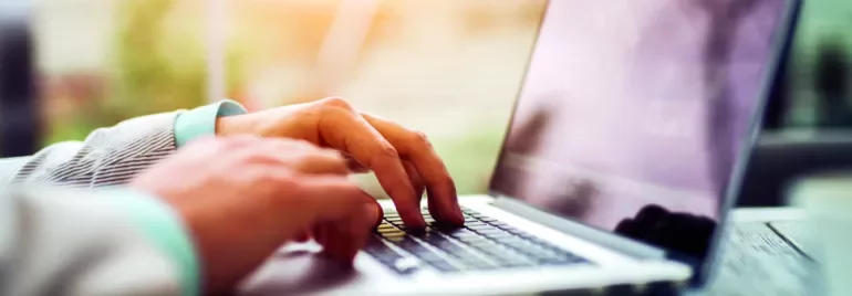 Person typing on a laptop at a desk, close-up view of the hands and keyboard.