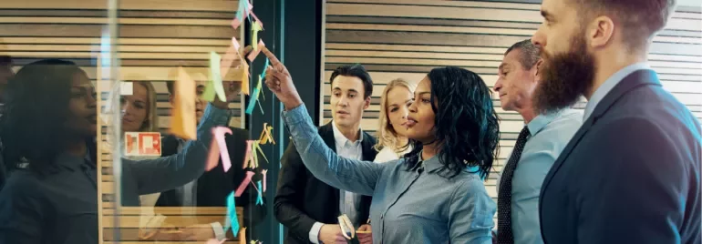 Business team collaborating with sticky notes on glass wall.