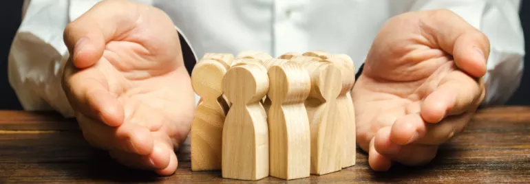Wooden figurines representing people encircled by protective hands on a wooden table.