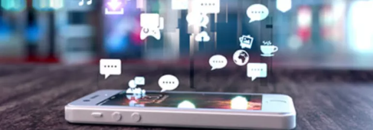 Smartphone with social media icons floating above its screen on a wooden table.