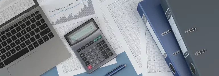 Laptop, calculator, and files on a desk with financial charts and documents.