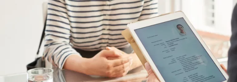 Person holding a tablet showing a resume during an interview at a glass table.