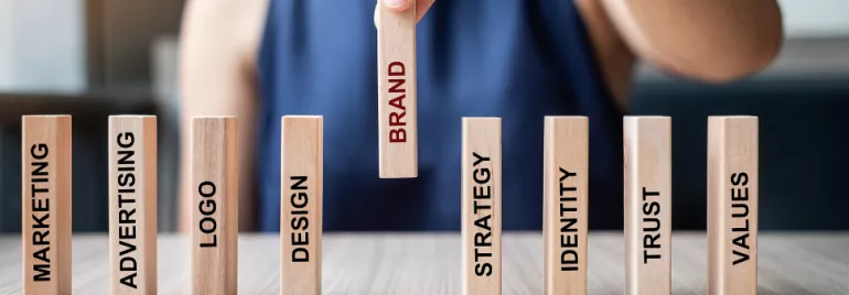 Hand holding a block with the word 'Brand' among other business-related blocks on a table.