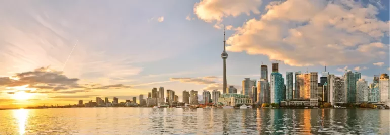 Panoramic view of a city skyline with a tall tower at sunset, reflecting on the water.