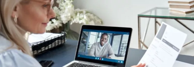 Woman holding a resume during a video call with a man on a laptop.