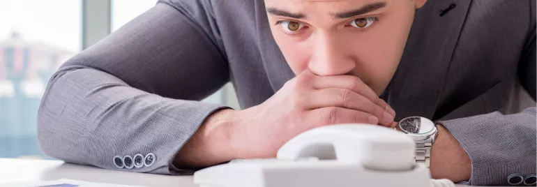 Man in a suit looks anxiously at a telephone on a desk.