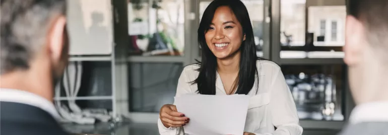 Smiling woman in a white blouse holding papers during a meeting.