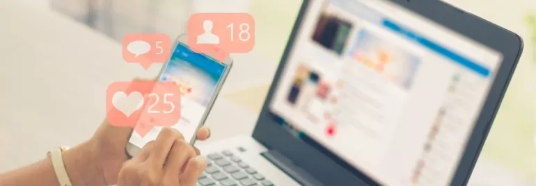 Person using smartphone with social media notifications near a laptop.