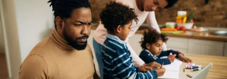 Family working together at a kitchen table with a laptop and books.