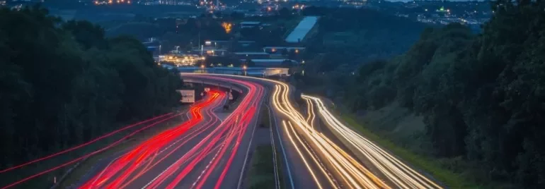 Night view of highway with light trails from vehicles under a dark, starless sky.