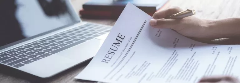 Person reviewing a resume near a laptop.
