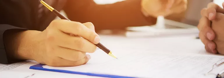 Person writing on a clipboard with a pen during a meeting.