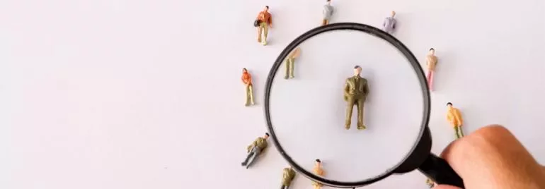 Magnifying glass over mini figures, focusing on one person.