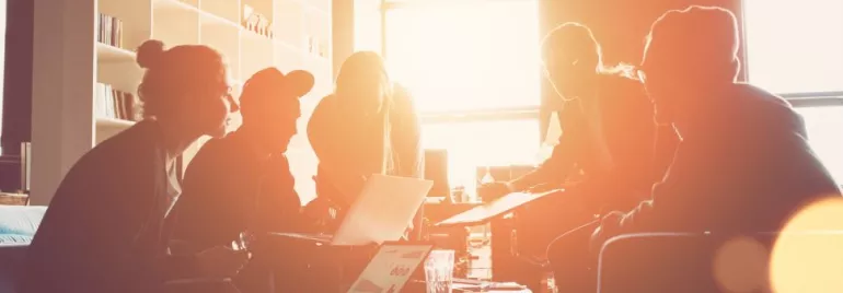 Group of people collaborating on laptops in a sunlit office.