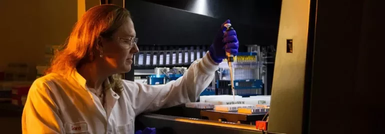 Scientist in lab coat using pipette in laboratory setting.