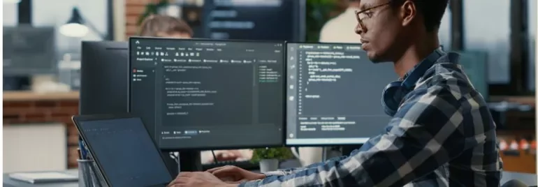 Person coding at a desk with multiple monitors displaying code.