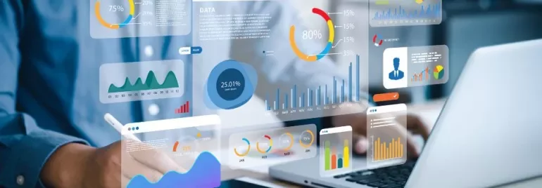Person analyzing data visualizations on a laptop with graphs and charts displayed on a transparent screen.