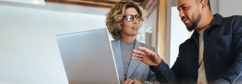 Two people discussing work at a desk with a laptop.