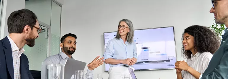 A diverse group of professionals in a meeting room discussing and smiling.