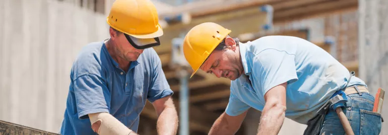 Two construction workers wearing hard hats working on a building site.