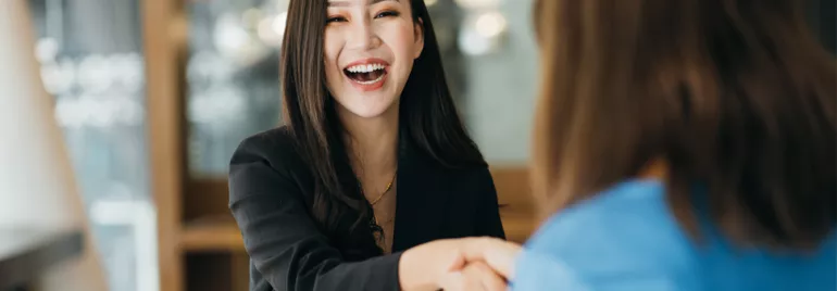 Woman in a black blazer smiling and shaking hands with another person.