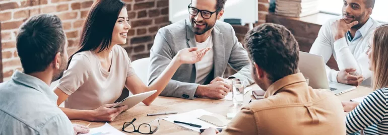 Team having a lively discussion around a wooden table in a modern office.