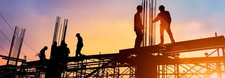 Silhouette of construction workers on scaffolding at sunset.