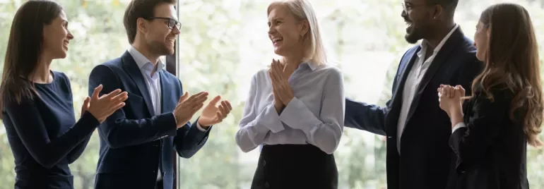 Group of colleagues clapping and celebrating together indoors.