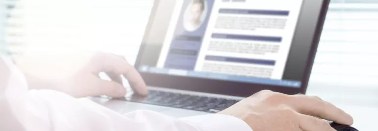 Person reviewing a resume on a laptop screen, hands resting on the keyboard.