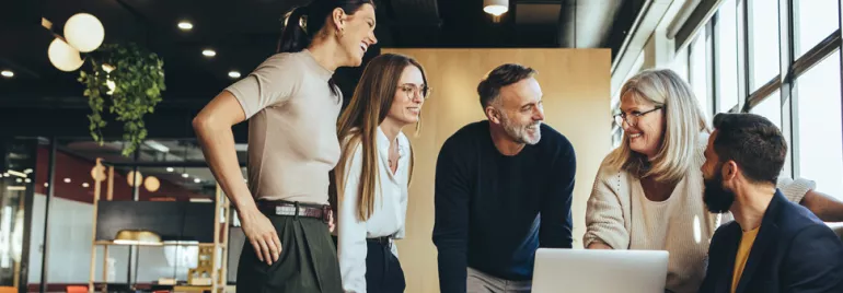 A diverse group of professionals having a meeting around a laptop in a modern office.