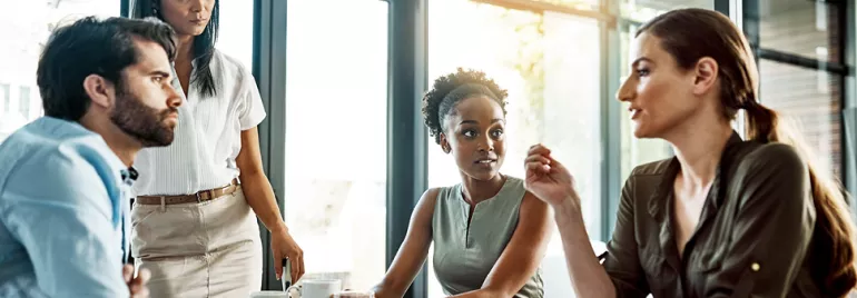 Four colleagues discussing at a meeting table in a bright office.