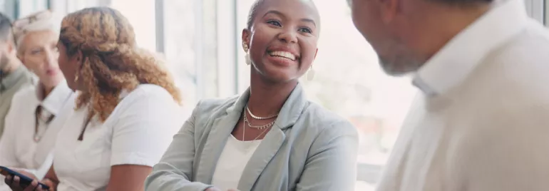 Smiling woman in a suit shaking hands with a man in an office setting.