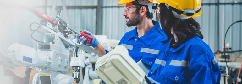 Two engineers in blue uniforms and helmets work with industrial machinery.