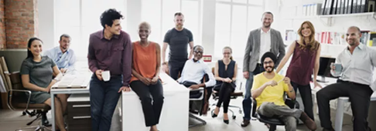 A diverse group of ten people in an office setting, smiling and posing together.