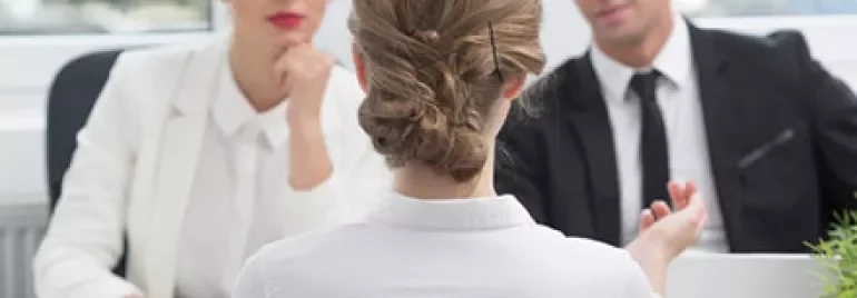 Person in a white shirt facing two interviewers across a table.