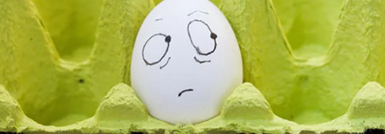 Egg with a drawn face showing confusion in a green egg carton.